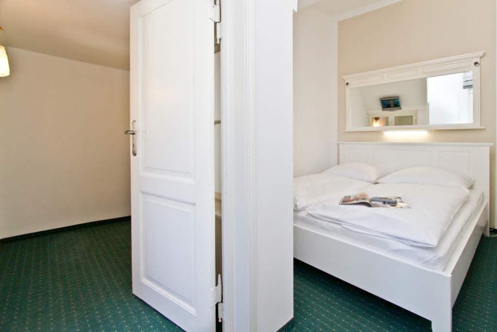 Een hotelkamer met een bed, een witte deur, een spiegel boven het bed en een groen tapijt.