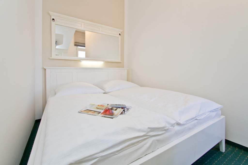 A single bed with white bedding, a bedside table, and a wall-mounted mirror.