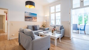 A modern living room with a grey sofa set, a white coffee table, and a large window providing natural light. - Villa Hartmann-Drewitz, App. 06 (Heringsdorf)