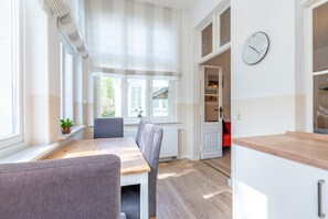 Ein helles Zimmer mit einem Holztisch, Stühlen, einer Heizung und einer Uhr an der Wand.
