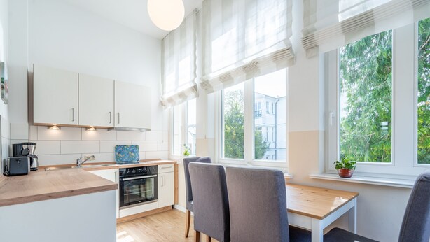 A modern kitchen with white cabinets, a wooden countertop, and a dining area with grey chairs. - Villa Hartmann-Drewitz, App. 06 (Heringsdorf)