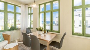 Spiseplads med et bord, stole og havudsigt gennem store vinduer.