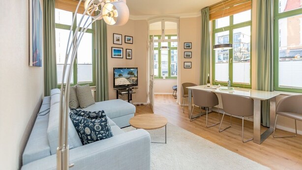 A modern living room with a sofa, a coffee table, a TV, and a dining area with chairs and a table. - Villa Frohsinn, app. 06 (Heringsdorf)