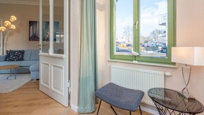 A room with a large window, a sofa, a small table, and a chair. - Villa Frohsinn, app. 06 (Heringsdorf)