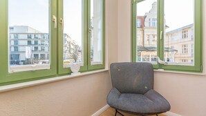 A room with a chair near a window with green frames, a white wall, and a view of buildings outside. - Villa Frohsinn, app. 06 (Heringsdorf)