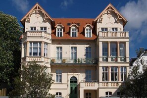 Un bâtiment historique à la façade symétrique, doté de grandes fenêtres et d’une entrée centrale avec une porte verte.