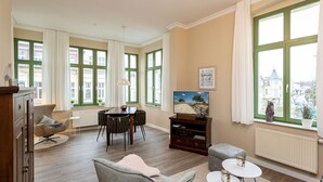 A spacious living room with a dining area, large windows with green frames, a fireplace, and a view of the city.