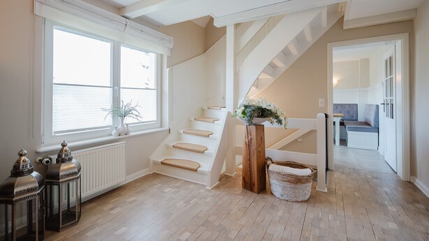 Eine Treppe mit Holzsitzstufen und einem weißen Geländer, die zu einem Zwischenpodest mit einer Pflanze und einem Korb führt.
