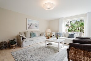 A living room with a sofa, a coffee table, a lamp, and a window with a view of trees.