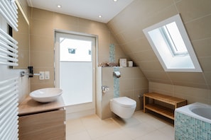 Een moderne badkamer met dakraam, ligbad, toilet en wastafelmeubel met een wastafel.