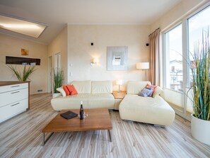 Una sala de estar moderna con un sofá, una mesa de centro y una lámpara. Hay una ventana con cortinas, una planta y un aplique de pared.