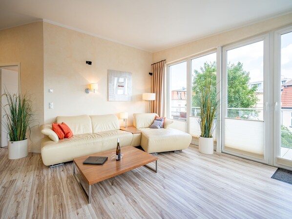 Een moderne woonkamer met een beige bank, een houten salontafel en grote ramen met uitzicht op de stad.