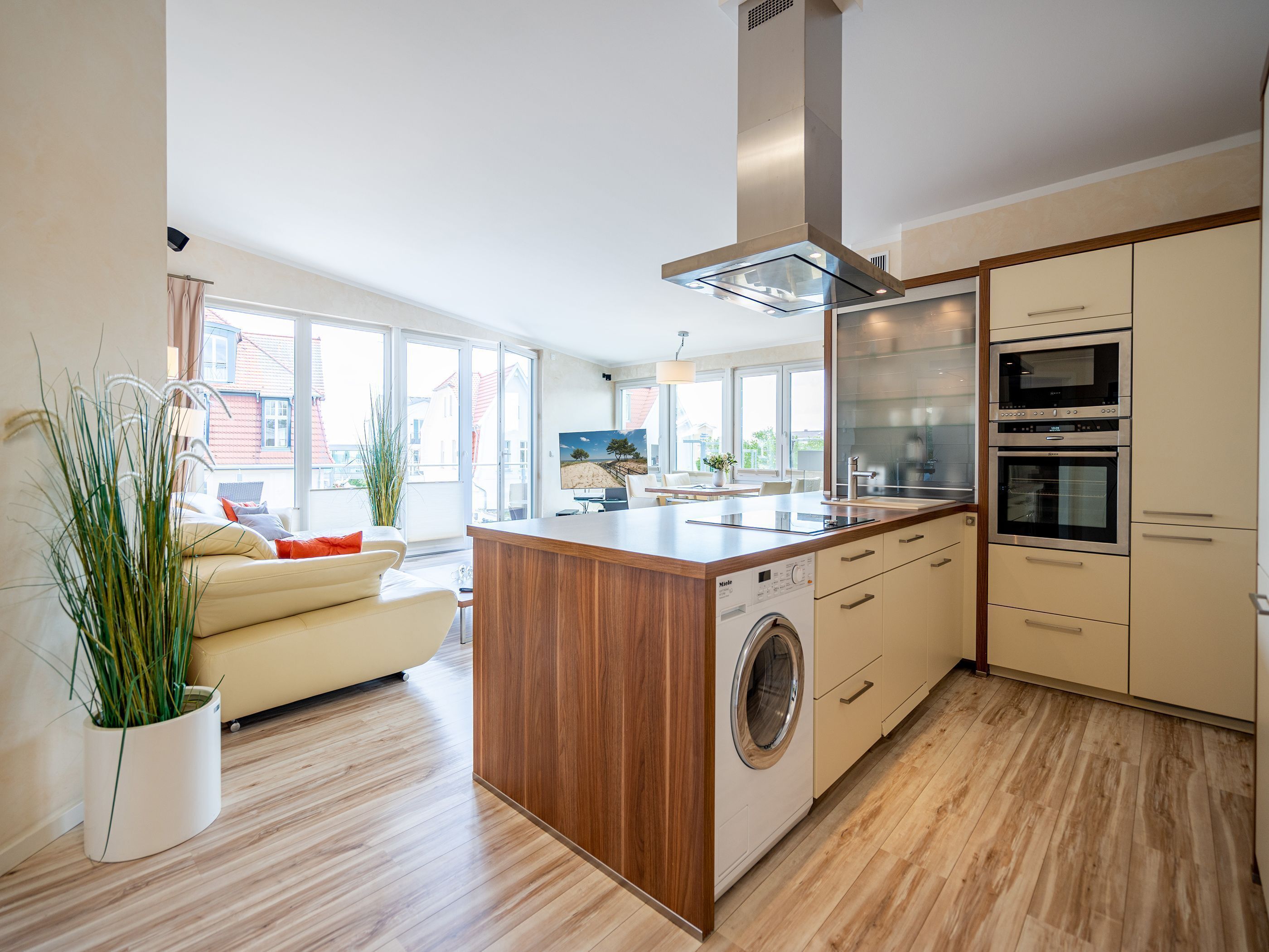 A modern kitchen with a central island, built-in oven, and a large window offering a view of the outside.