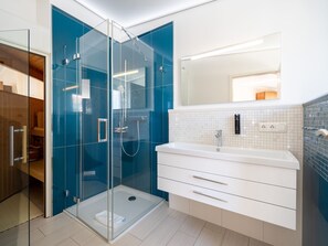 Een moderne badkamer met een douche met glazen wand, een wit wastafelmeubel met spiegel en een betegelde achterwand.