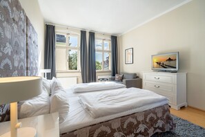 Quarto de hotel com cama, televisão, escrivaninha e janela com cortinas.