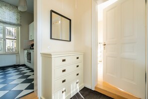 A room with a checkered floor, a white dresser with drawers, a mirror on the wall, and a white door. - Villa Schlossbauer, App. 06 Remise (Heringsdorf)