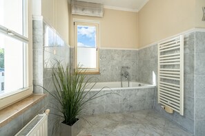 A bathroom with a bathtub, a window, a radiator, and a potted plant. - Villa Schlossbauer, App. 06 Remise (Heringsdorf)