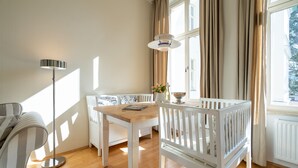 A room with a wooden table, white crib, and a sofa. - Villa Schlossbauer, App. 06 Remise (Heringsdorf)