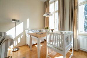A room with a wooden table, white crib, and a sofa. - Villa Schlossbauer, App. 06 Remise (Heringsdorf)