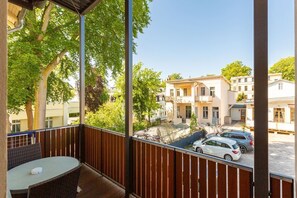 Ein Balkon mit Korbmöbeln, Blick auf eine Wohnstraße mit parkenden Autos und Gebäuden im Hintergrund.