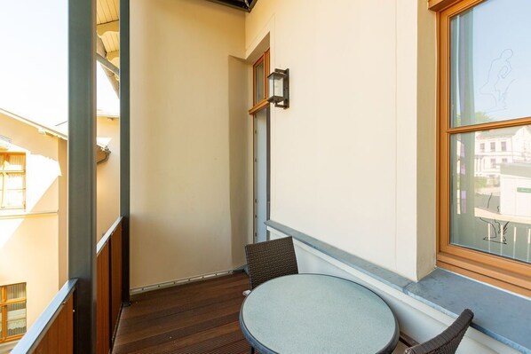 A balcony with a round table and two chairs, a window with a view of buildings, and a wall-mounted light fixture.