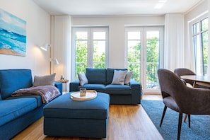 A modern living room with a blue sofa, ottoman, and a dining area with chairs and a table. - Beach house, App. 08, Germany (Heringsdorf)