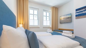 Habitación de hotel con dos camas, un ventanal grande, un cuadro de una playa y una lámpara.