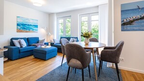 Una sala de estar moderna con un sofá azul, una mesa de comedor con cuatro sillas y un ventanal con vistas al mar.