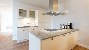 Une cuisine moderne avec des meubles blancs, un plan de travail en granit et une hotte de cuisinière en acier inoxydable.