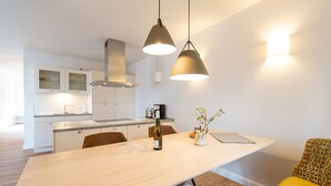 Une cuisine moderne avec une table à manger en bois, des luminaires suspendus et une chaise jaune.