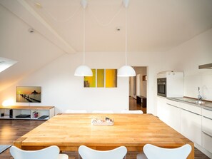 Une cuisine moderne avec des meubles blancs, une table à manger en bois et des luminaires suspendus.