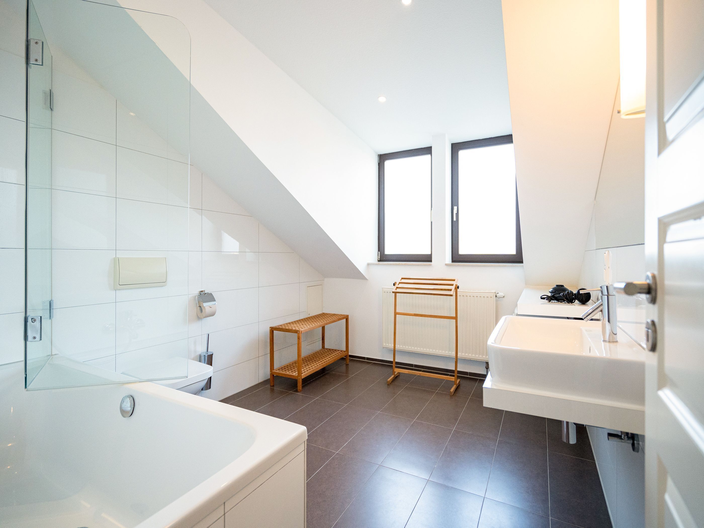 A modern bathroom with a bathtub, a wooden shelf, a radiator, and a window.