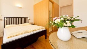 A bedroom with a bed, a bedside table with a vase of flowers, a telephone, and a wooden door. - Villa Astrid, T6 Stralsund (Heringsdorf)