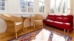Ein Zimmer mit einer roten Couch, Korbsesseln, einem kleinen Tisch und einem farbenfrohen Teppich.