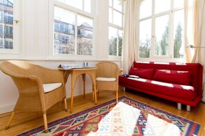 A room with a red sofa, wicker chairs, a small table, and a colorful rug.