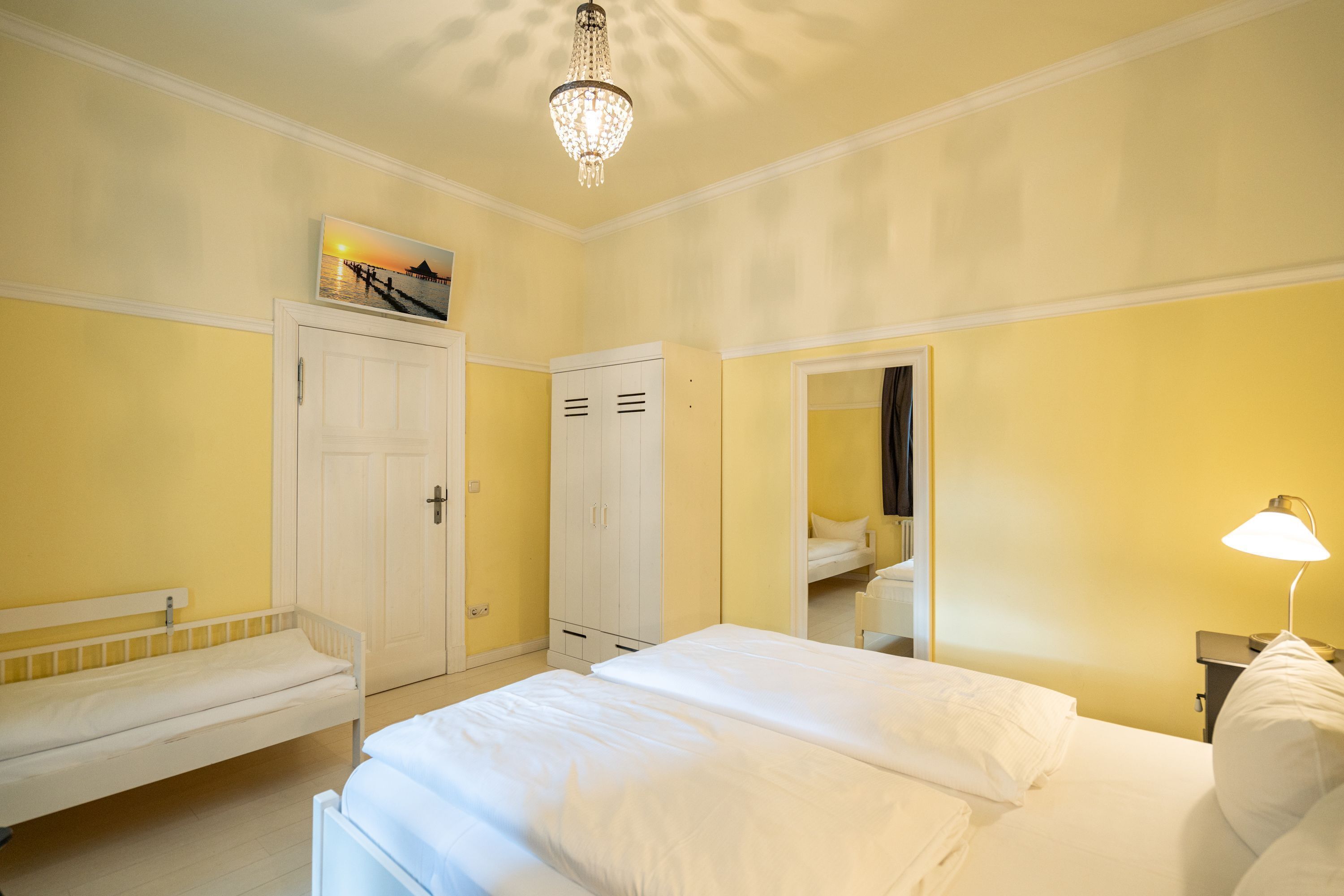 Ein Hotelzimmer mit Bett, Sitzbank, Kleiderschrank, Spiegel und einer Kandelaber.