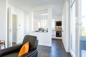Uma sala de estar moderna com um sofá de couro preto e uma porta de vidro que dá para uma cozinha.