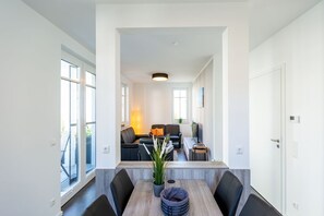 A modern dining area with a long table, black chairs, and a potted plant. There is a sofa and a TV in the background. - Beach house, App. 03, Germany (Heringsdorf)
