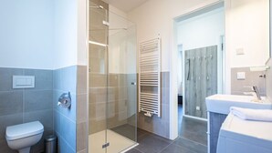 Een moderne badkamer met een douchecabine van glas, een wit toilet, een handdoekhouder en een wastafel met spiegel.