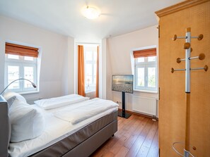 Quarto com cama, televisão, radiador e janelas com cortinas.