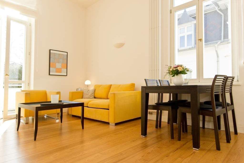 Een woonkamer met een gele bank, een salontafel en een eettafel met stoelen.