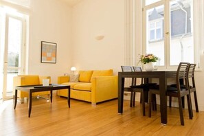 Un salon avec un canapé jaune, une table basse et une table à manger avec des chaises.