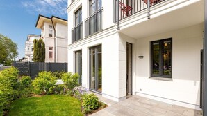 Ein modernes, zweistöckiges Gebäude mit weißer Fassade, großen Fenstern und einem kleinen Garten mit verschiedenen Pflanzen.