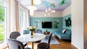 Ein modernes Wohnzimmer mit einem runden Marmortisch, grauen Polsterstühlen, einem blauen Sofa und einem an der Wand befestigten Flachbildfernseher.