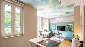 Eine moderne Küche mit Einbauherd, ein Essbereich mit Tisch und Stühlen sowie ein Wohnbereich mit Sofa und Bildern an der Wand.