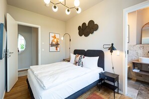 A bedroom with a bed, bedside table, lamp, and artwork on the wall.
