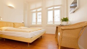 Een slaapkamer met een bed, een stoel, een klein tafeltje met een plant en een raam.