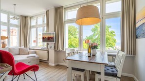 A spacious living room with a sofa, red chair, dining table, and large windows offering a view of the sea. - Rolandseck, App. 3, Germany (Heringsdorf)