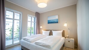 A hotel room with a large bed, two bedside tables, a nightstand, a lamp, a painting, and a view through the window. - Quartier Frohsinn, app. 04b (Heringsdorf)