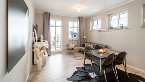 A modern living room with a glass dining table, leather sofa, and a large flat-screen TV mounted on the wall. - Quartier Frohsinn, app. 04b (Heringsdorf)